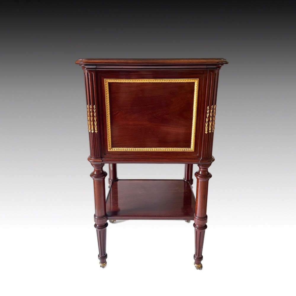 A French Louis XVI style mahogany bedside cabinet featuring two drawers framed with beaded ormolu trim, fluted corner columns, a lower tier shelf, and turned legs with brass castors. View VII
