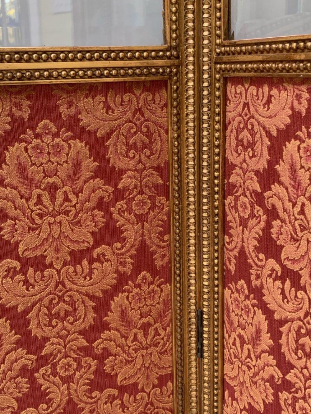 A Victorian four-fold screen featuring carved giltwood frames with arched tops, upper neutral panels, lower red and gold damask fabric panels, and brass hinges. View III