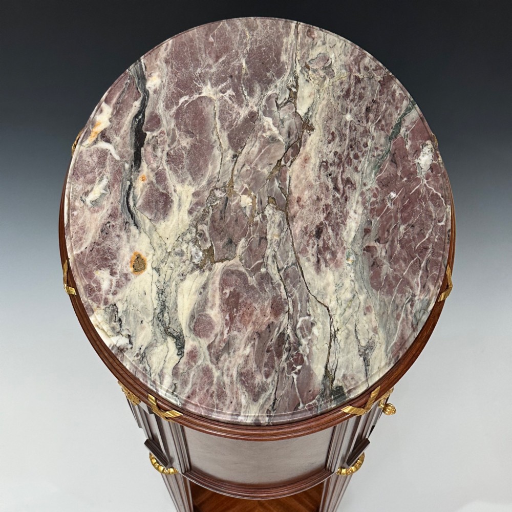 An oval French mahogany table de nuit featuring a grey marble top, gilt-bronze mounts, single drawer, cupboard door, and fluted legs with an undertier. View III