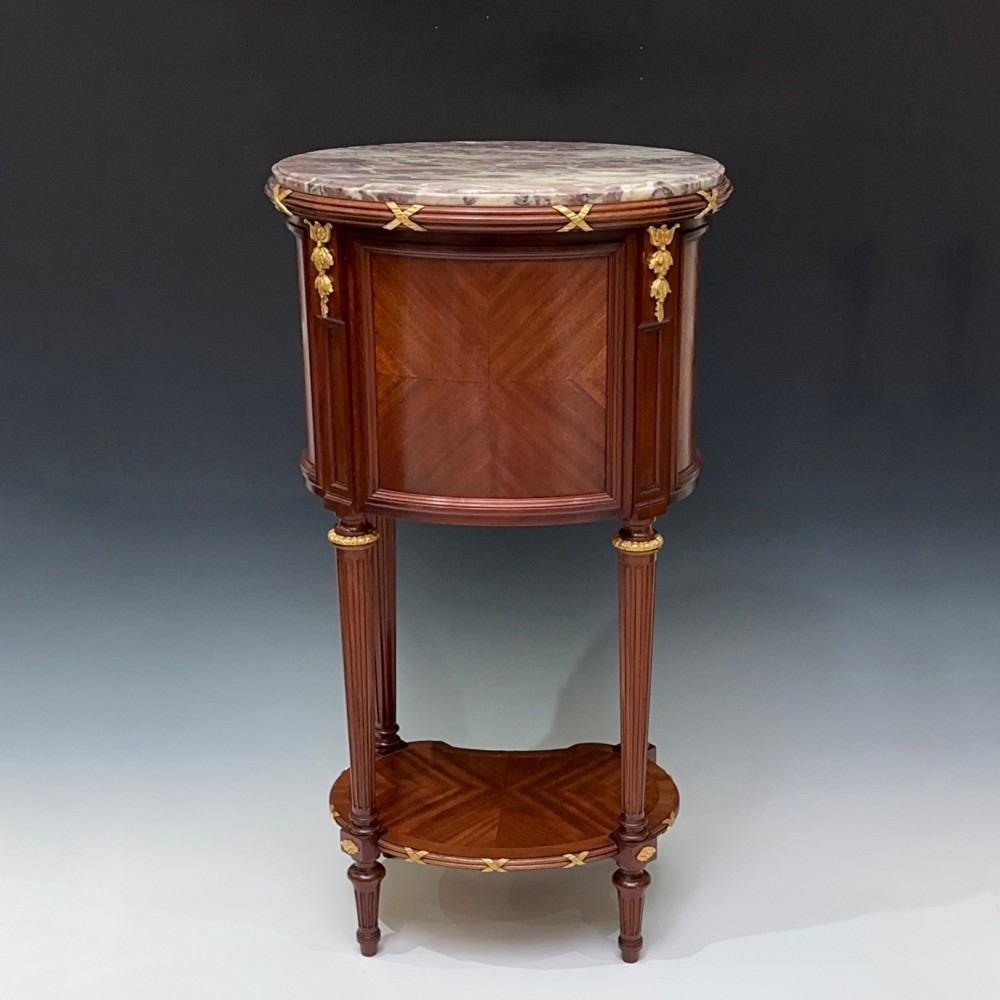 An oval French mahogany table de nuit featuring a grey marble top, gilt-bronze mounts, single drawer, cupboard door, and fluted legs with an undertier. View VIII