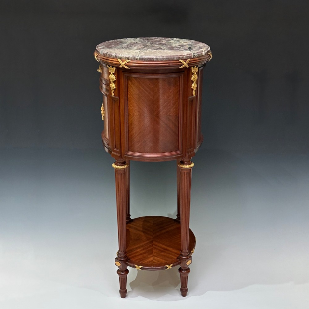 An oval French mahogany table de nuit featuring a grey marble top, gilt-bronze mounts, single drawer, cupboard door, and fluted legs with an undertier. View IX