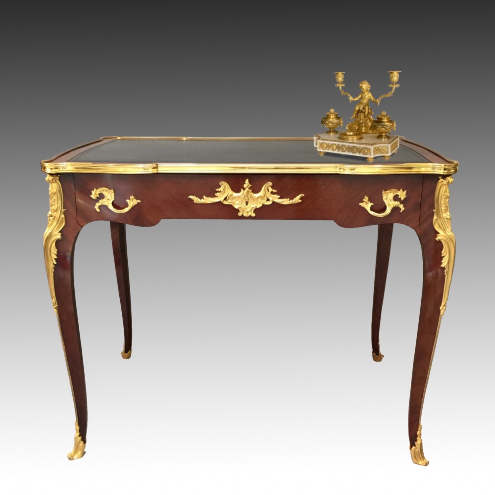 A French Louis XV style bureau plat crafted from dark polished wood with serpentine cabriole legs, elaborate gilt-bronze ormolu mounts, and a black leather writing top. View II