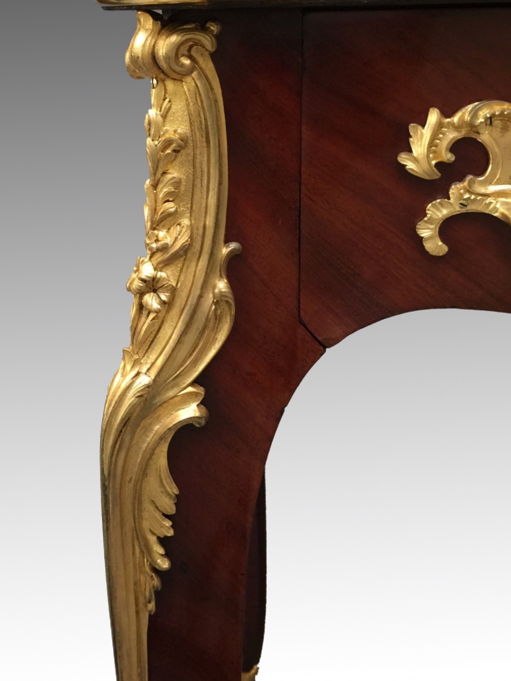 A French Louis XV style bureau plat crafted from dark polished wood with serpentine cabriole legs, elaborate gilt-bronze ormolu mounts, and a black leather writing top. View III