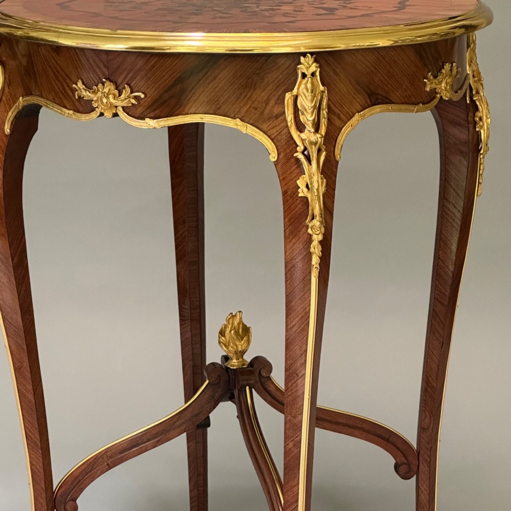 A round French kingwood occasional table featuring floral marquetry inlay, gilded ormolu mounts, slender cabriole legs, and a central stretcher with a carved finial. View III