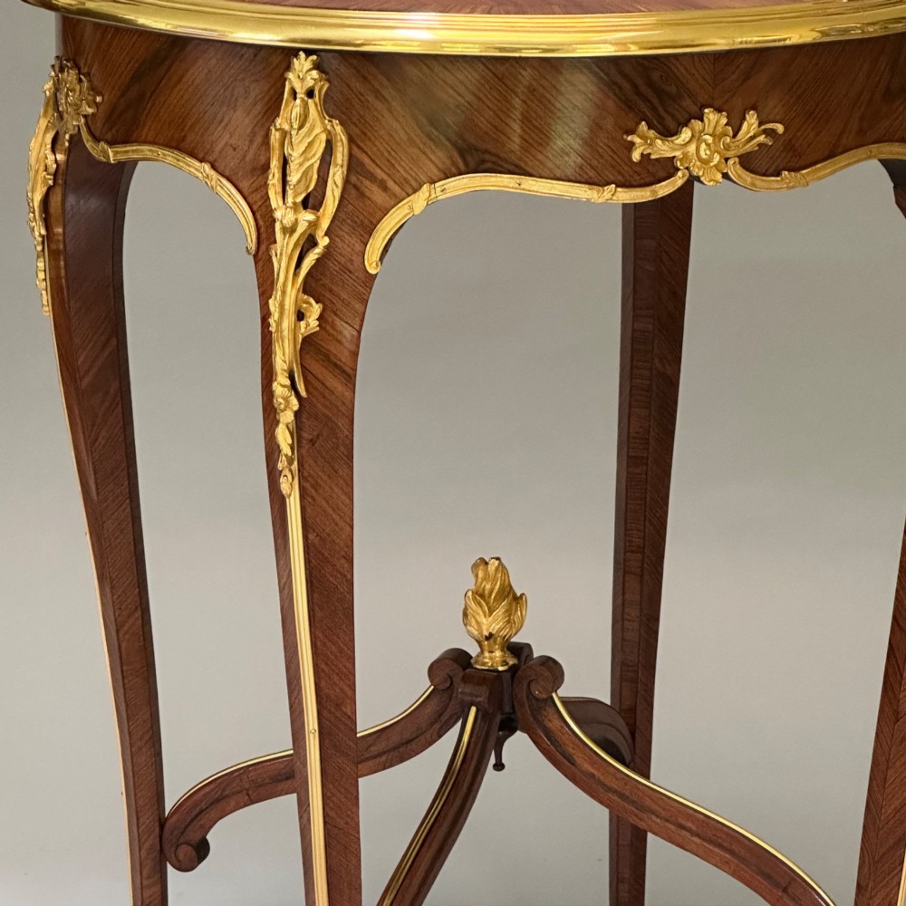 A round French kingwood occasional table featuring floral marquetry inlay, gilded ormolu mounts, slender cabriole legs, and a central stretcher with a carved finial. View IV