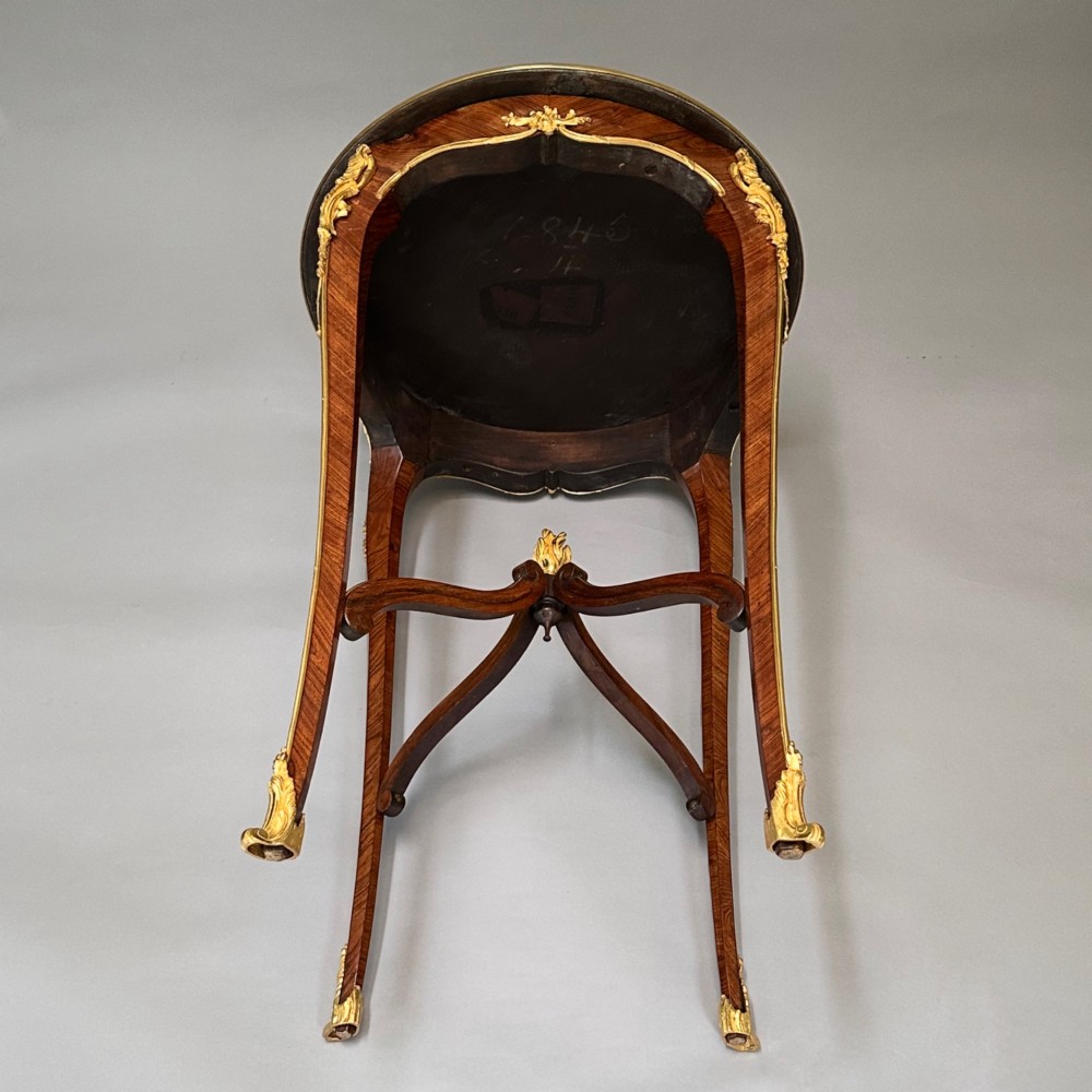 A round French kingwood occasional table featuring floral marquetry inlay, gilded ormolu mounts, slender cabriole legs, and a central stretcher with a carved finial. View VII