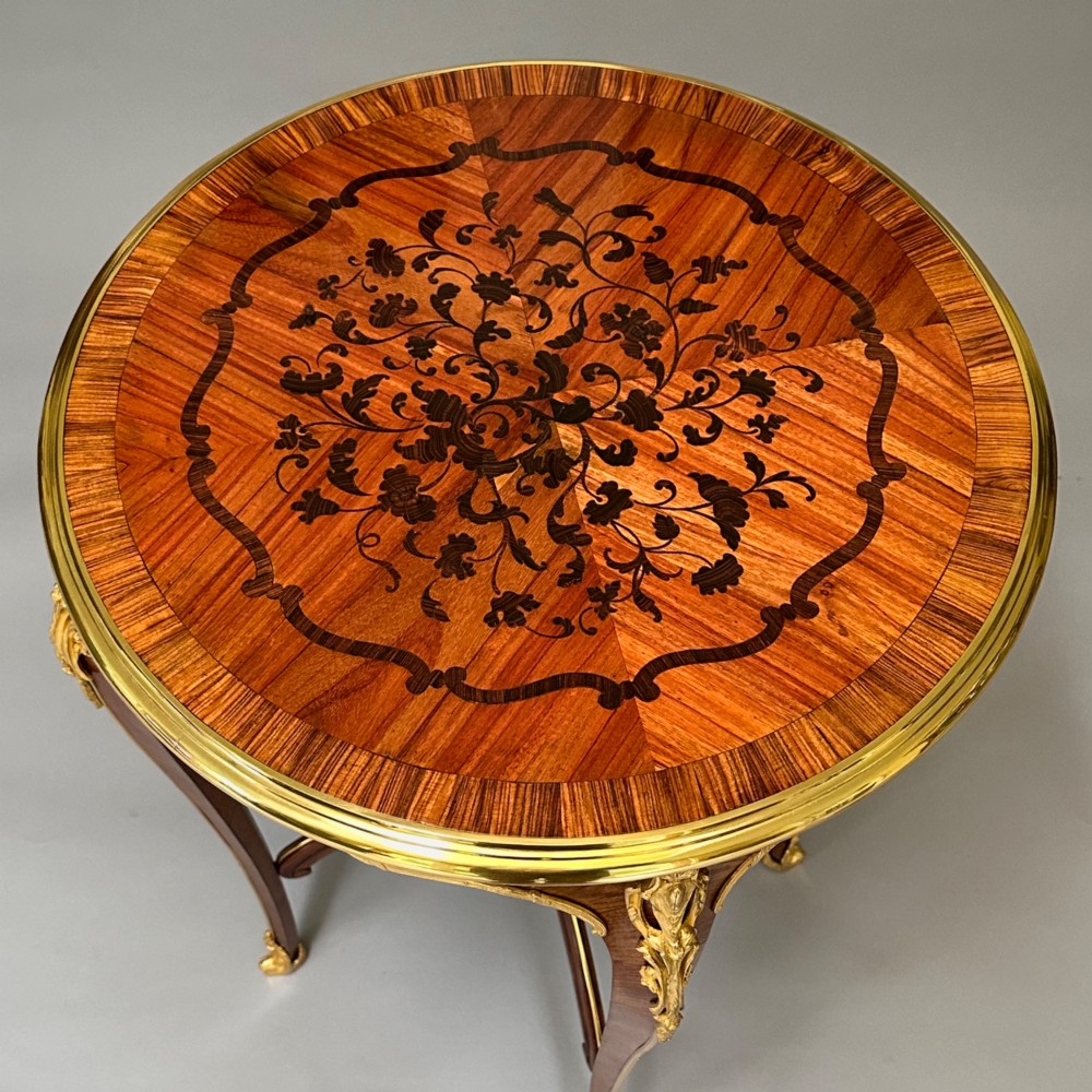 A round French kingwood occasional table featuring floral marquetry inlay, gilded ormolu mounts, slender cabriole legs, and a central stretcher with a carved finial. View VIII