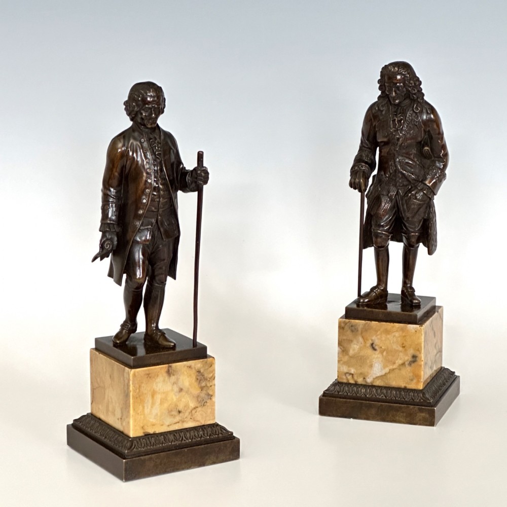 A pair of 19th-century French Restauration period patinated bronze statues of Voltaire and Rousseau mounted on yellow marble bases.