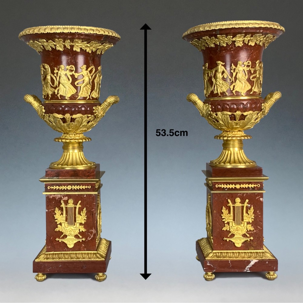A pair of French Empire style red marble urns featuring gilded bronze classical figure reliefs and mounted on square marble pedestals with lyre details. View II