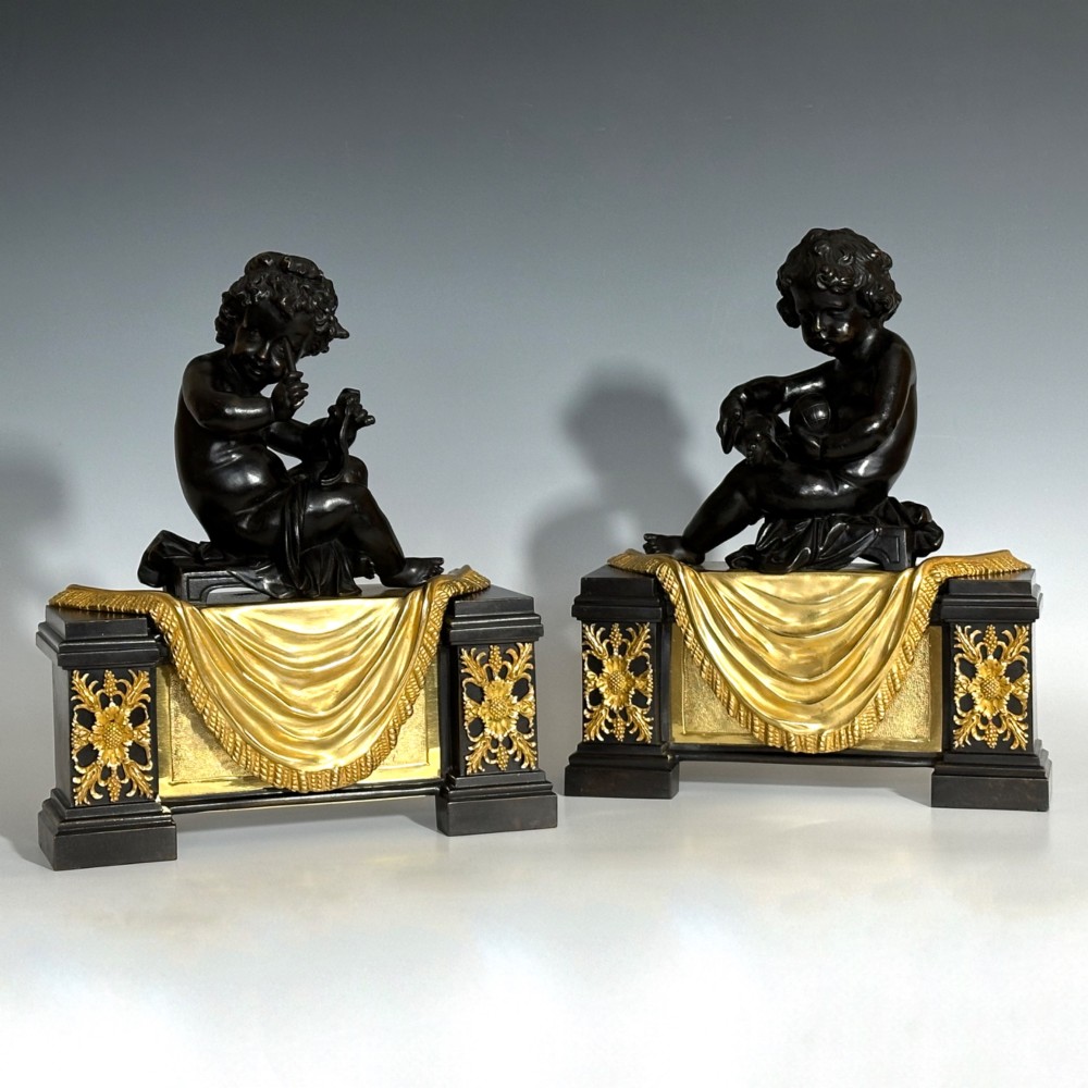 A pair of dark patinated bronze putti figures seated atop rectangular bases featuring gilt drapery and ornate floral side appliques. View II