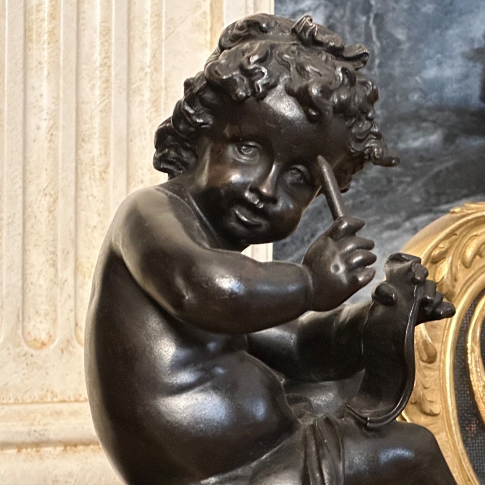 A pair of dark patinated bronze putti figures seated atop rectangular bases featuring gilt drapery and ornate floral side appliques. View VII