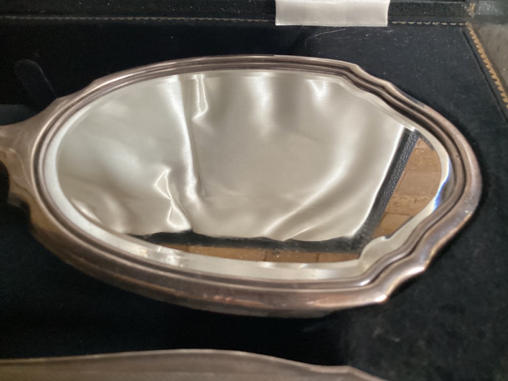 An antique hallmarked silver dressing table set including a hand mirror and two brushes with engine-turned detailing, resting inside a black velvet-lined presentation box. View IV
