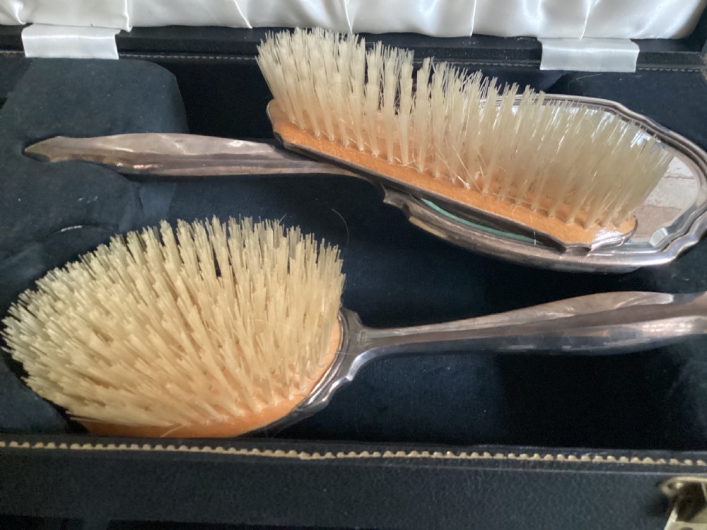 An antique hallmarked silver dressing table set including a hand mirror and two brushes with engine-turned detailing, resting inside a black velvet-lined presentation box. View VI