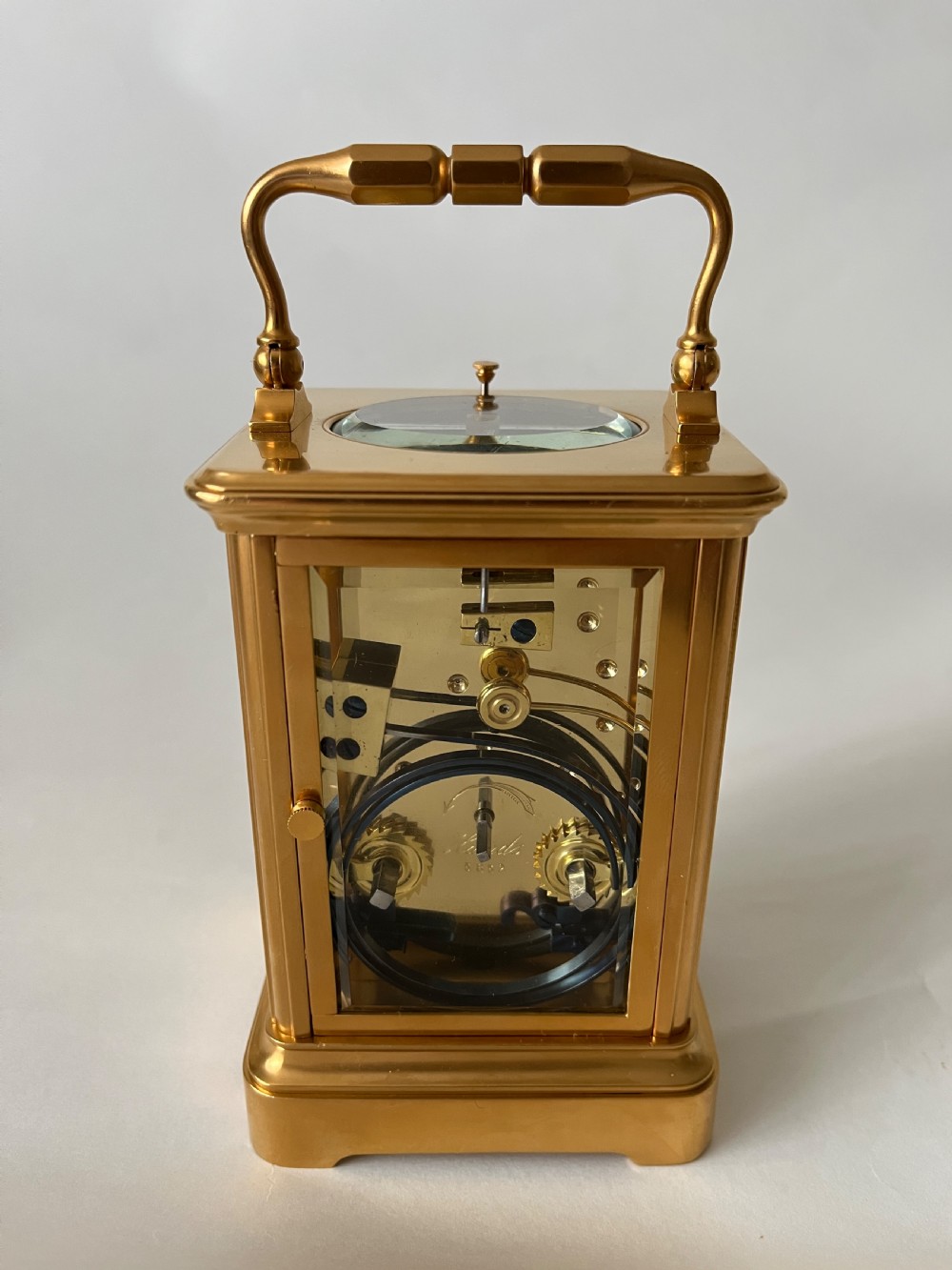 A rectangular gilt brass French repeating carriage clock with a top handle, glass side panels, and a white enamel dial with black Roman numerals. View II