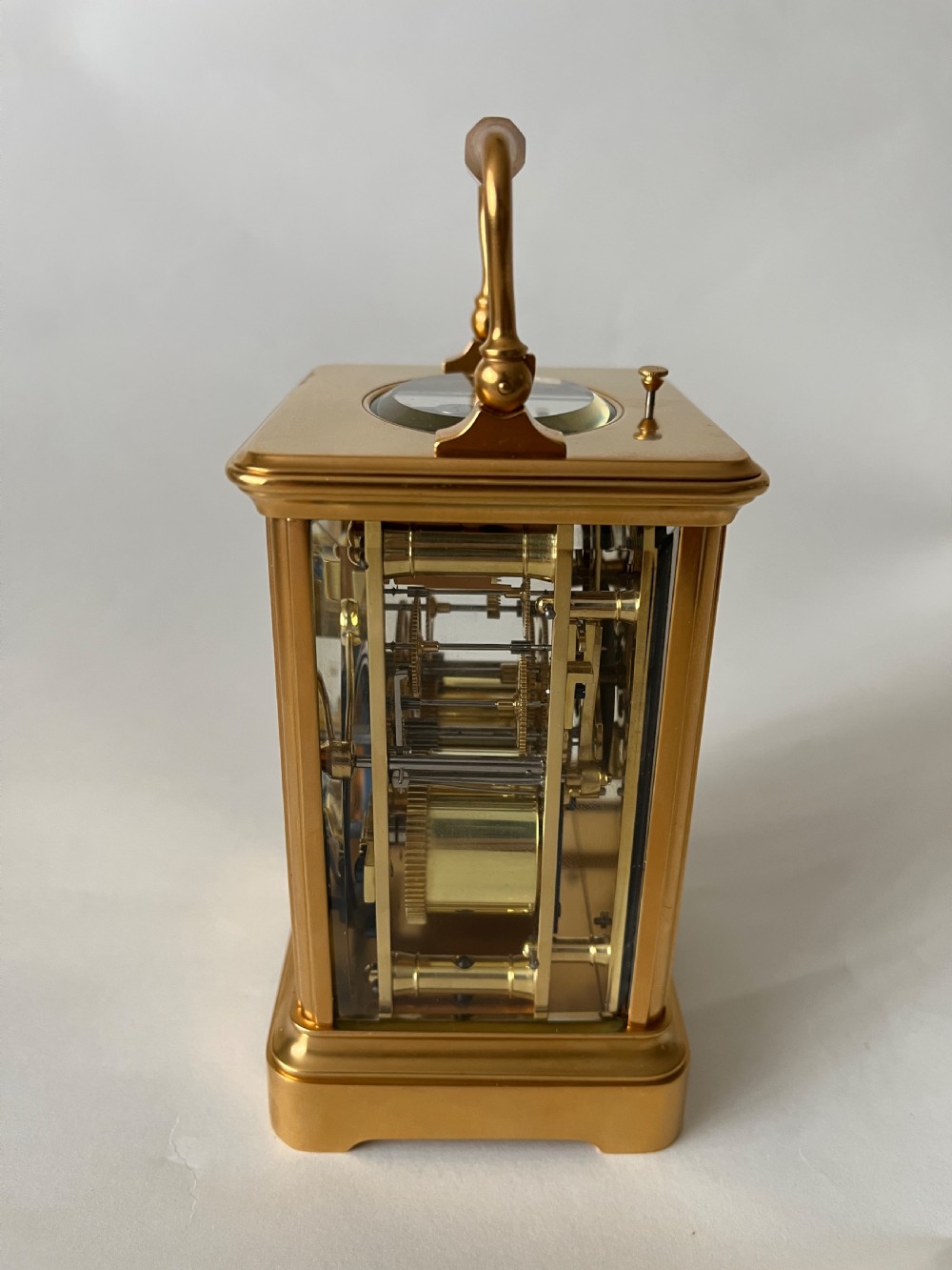 A rectangular gilt brass French repeating carriage clock with a top handle, glass side panels, and a white enamel dial with black Roman numerals. View IV