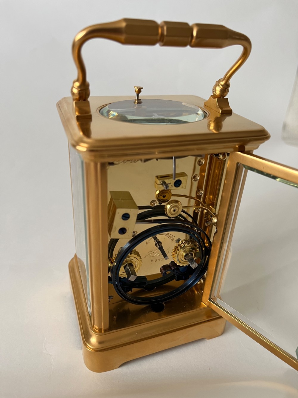 A rectangular gilt brass French repeating carriage clock with a top handle, glass side panels, and a white enamel dial with black Roman numerals. View V