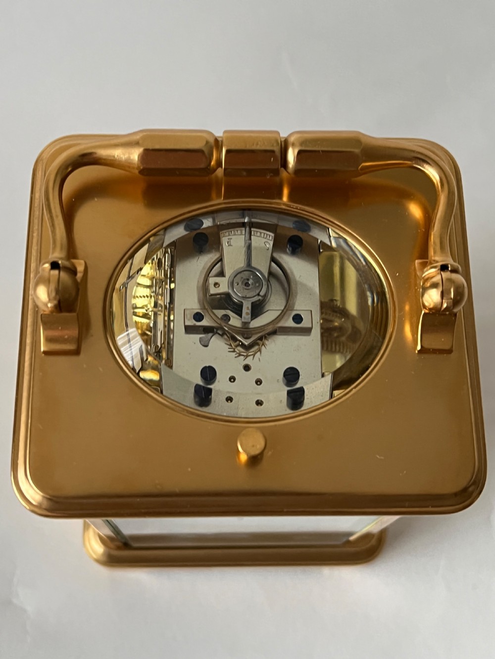 A rectangular gilt brass French repeating carriage clock with a top handle, glass side panels, and a white enamel dial with black Roman numerals. View VI