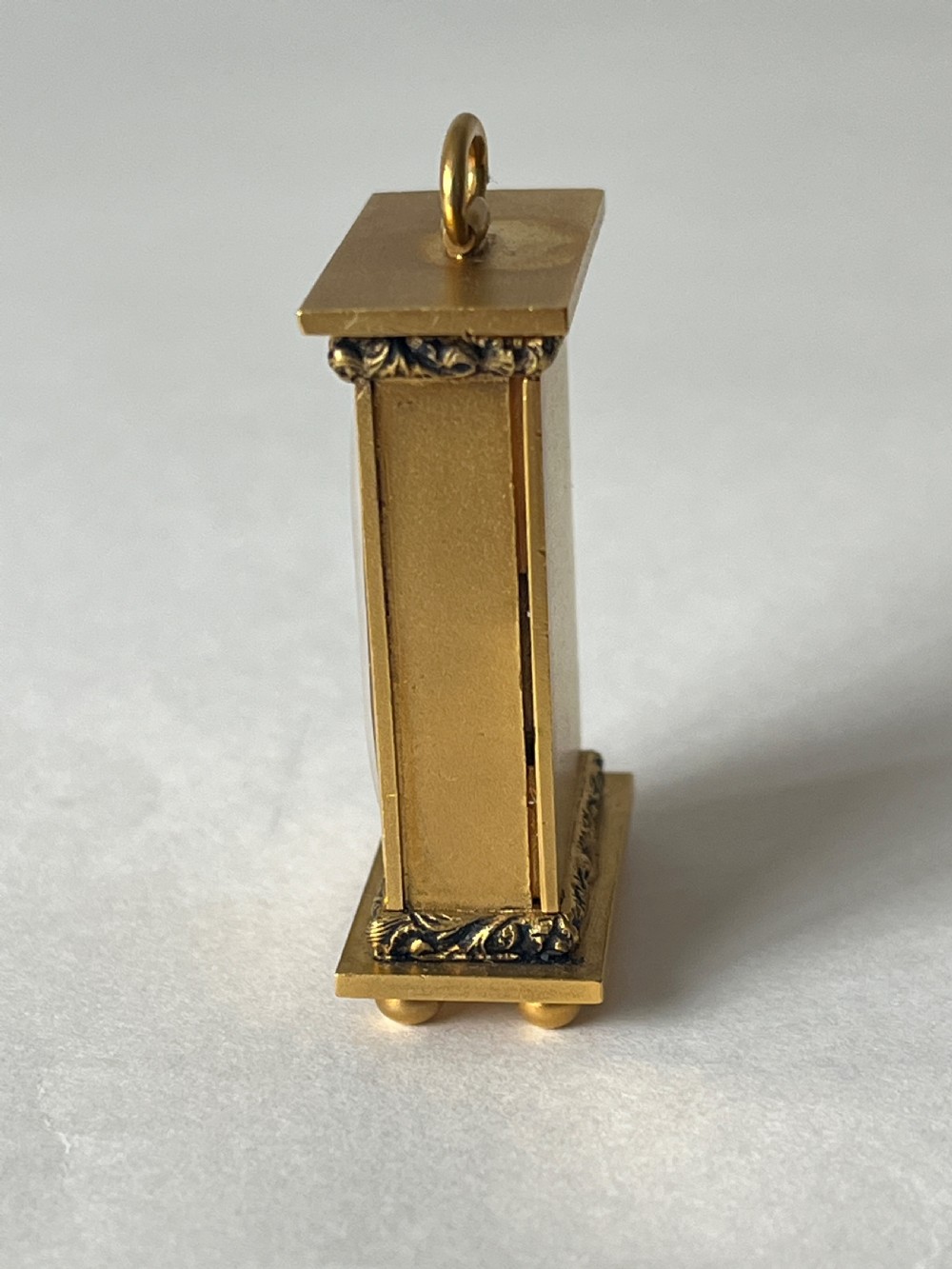 A small rectangular gilt brass Art Deco carriage clock featuring a top loop handle, chased floral borders, ball feet, and a golden guilloche dial with dark stylized numbers. View II