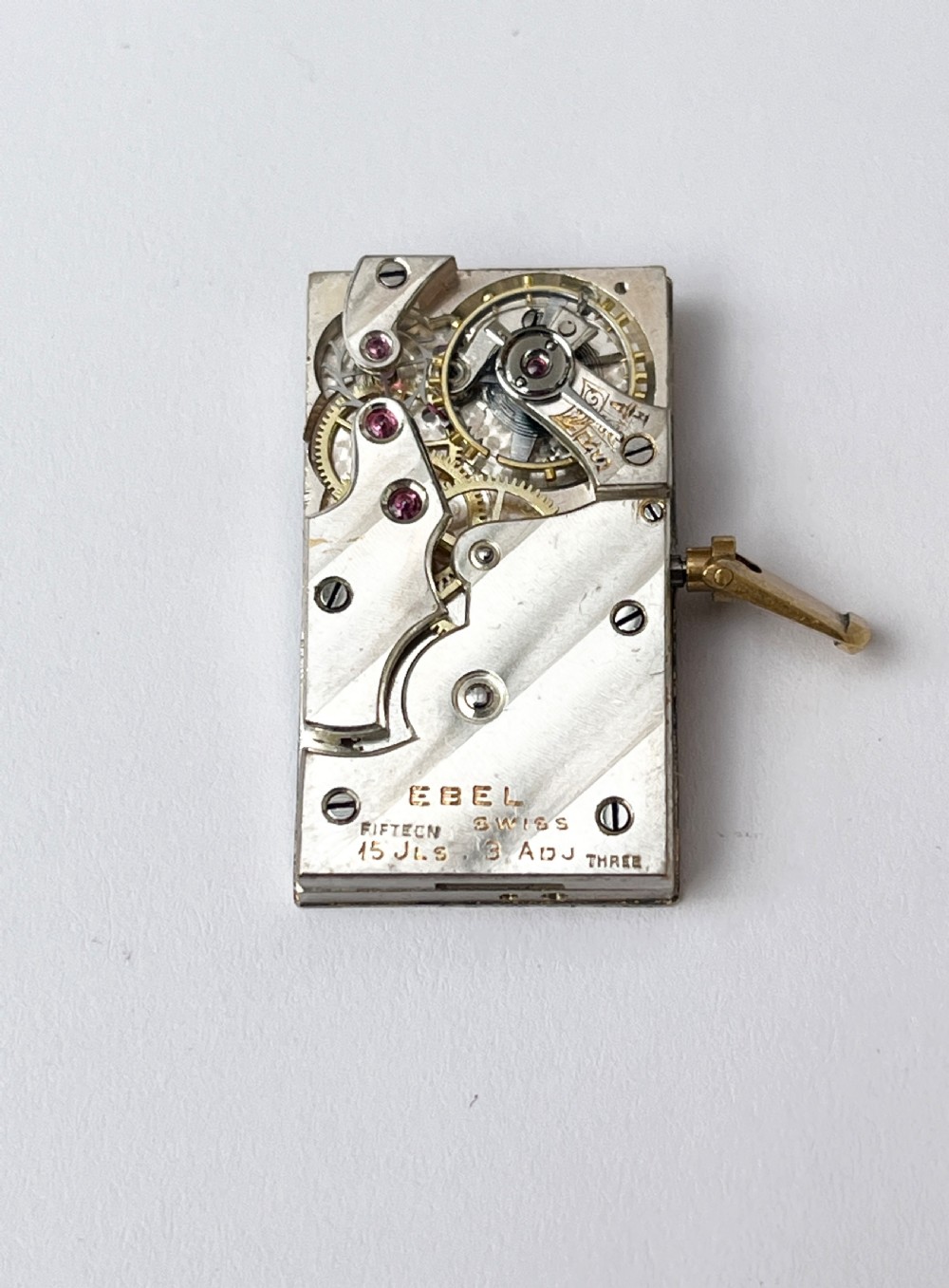 A small rectangular gilt brass Art Deco carriage clock featuring a top loop handle, chased floral borders, ball feet, and a golden guilloche dial with dark stylized numbers. View V