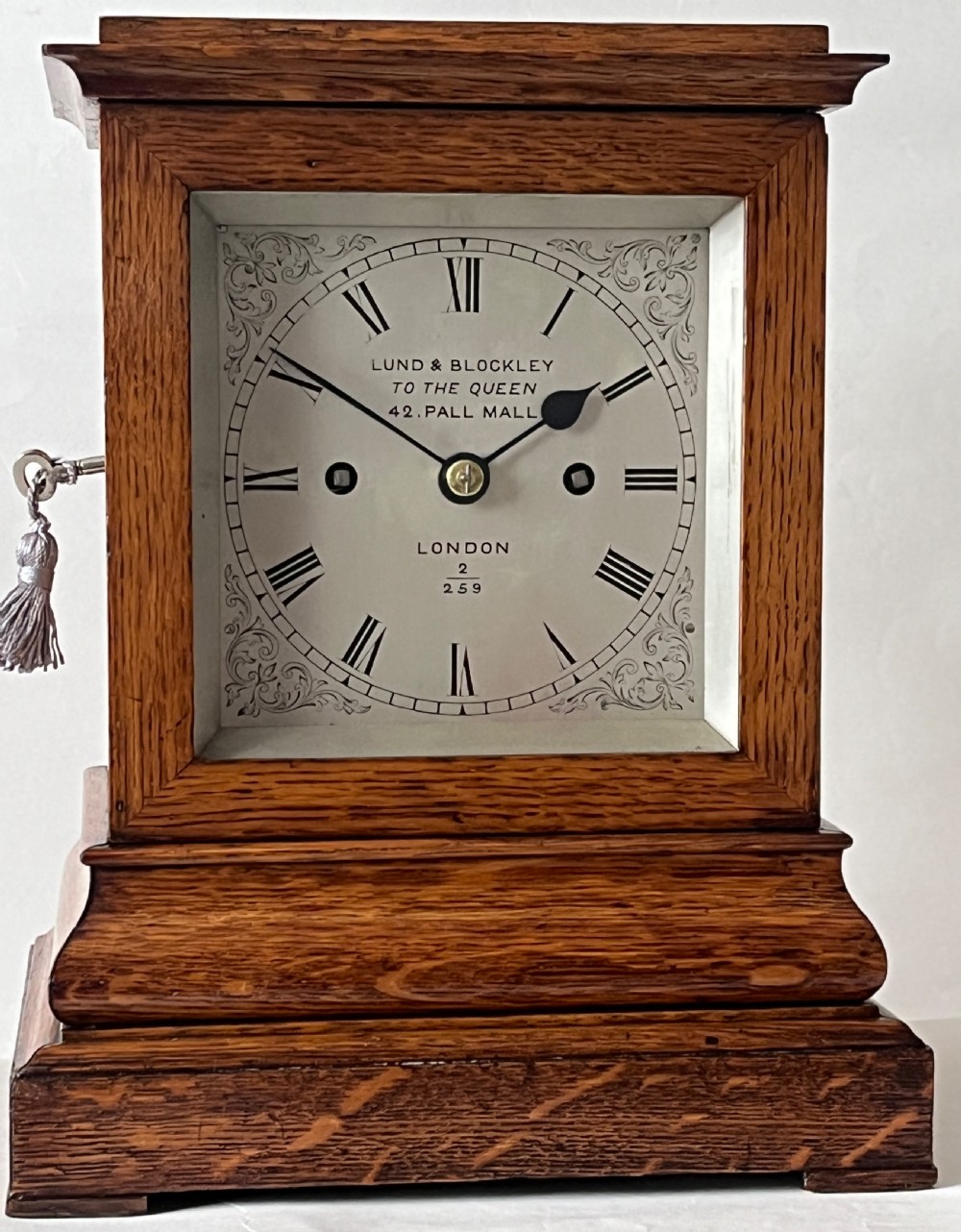 An antique Victorian oak library clock featuring a square silvered dial with Roman numerals and spandrel engravings set within a stepped wooden case.