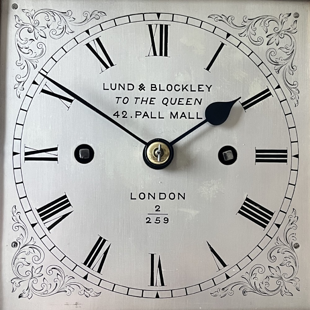 An antique Victorian oak library clock featuring a square silvered dial with Roman numerals and spandrel engravings set within a stepped wooden case. View VII
