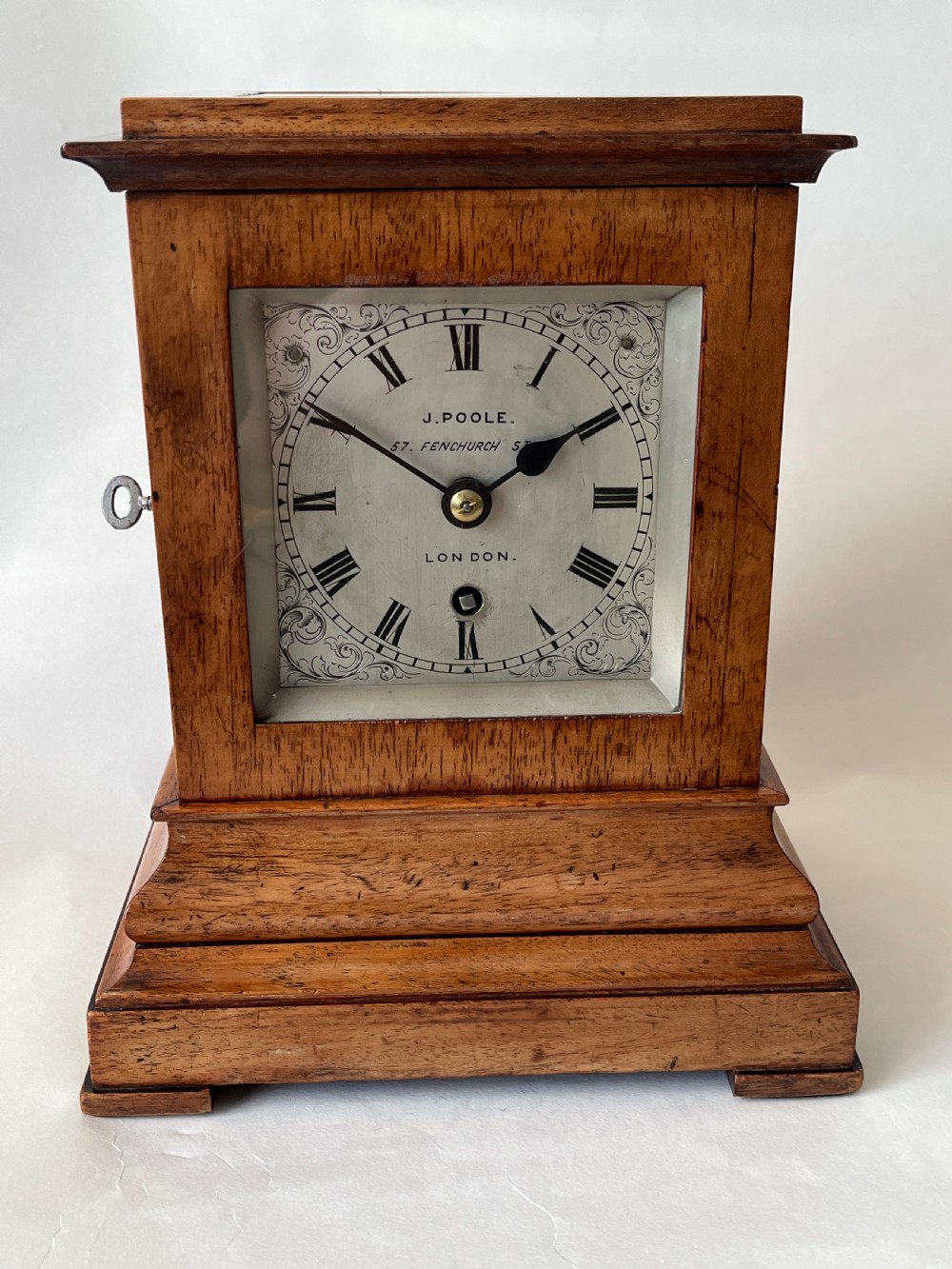 A Victorian mahogany library clock featuring a square timber case with a silvered engraved dial, black Roman numerals, and a key visible on the side.