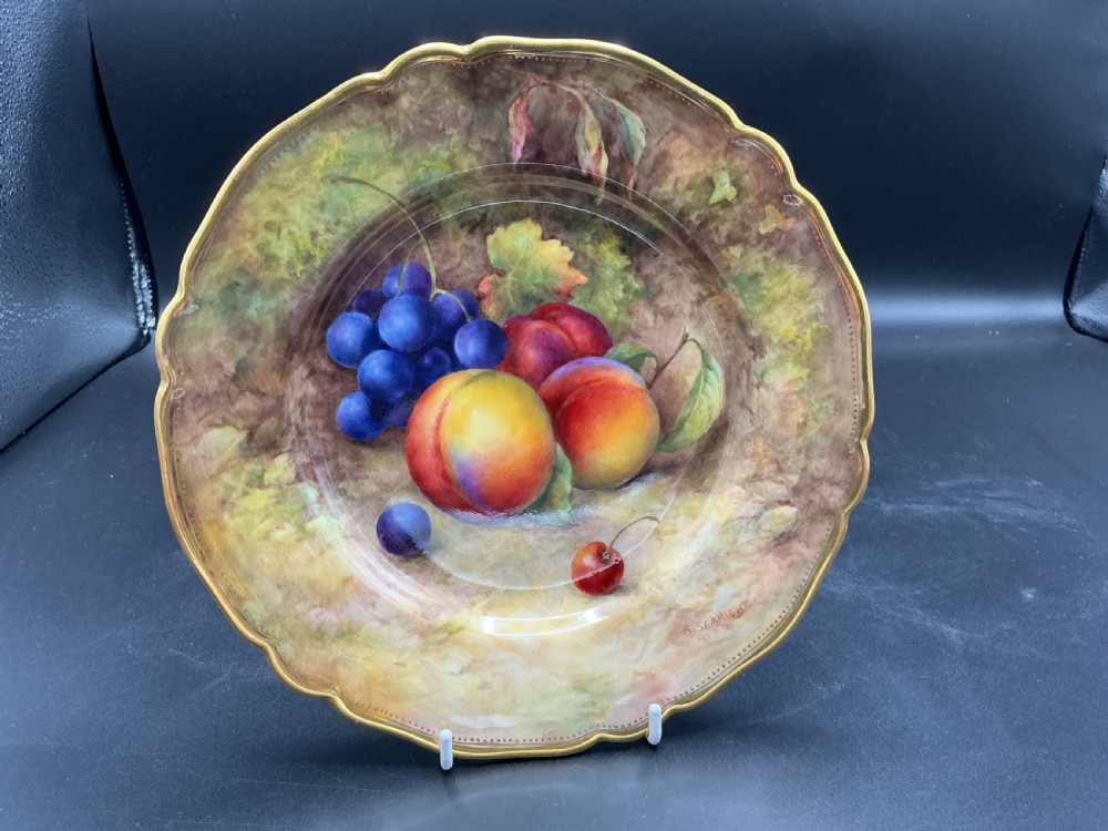 A circular bone china cabinet plate hand-painted with peaches and grapes against a mossy background, featuring a scalloped gilt rim.