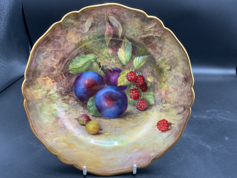 A circular Royal Worcester porcelain cabinet plate with a scalloped gilded rim, featuring a hand-painted still life of plums, raspberries, and gooseberries against a soft background.