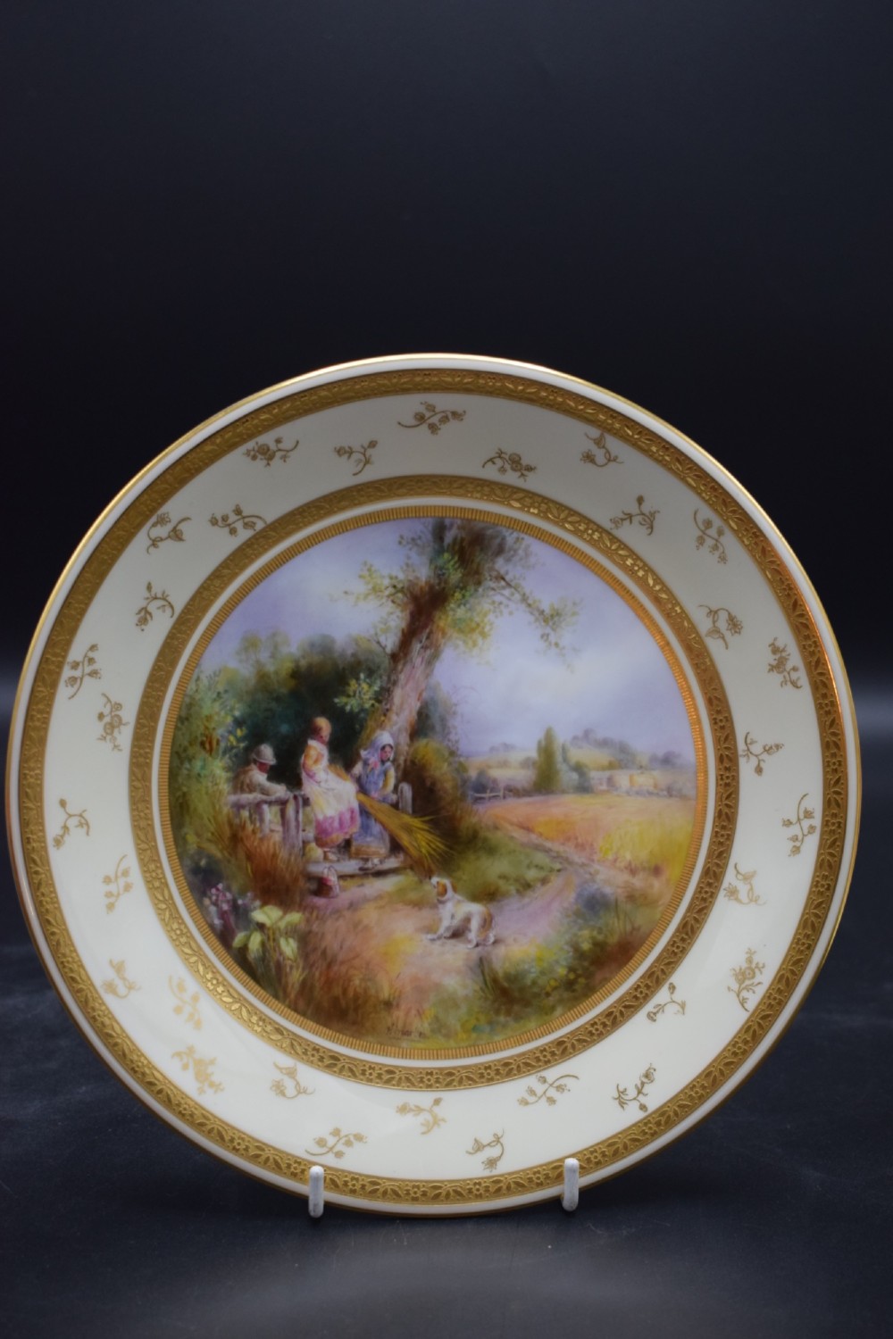 A pair of circular porcelain plates decorated with hand-painted pastoral landscapes and framed by wide cream borders with intricate gilded detailing. View II