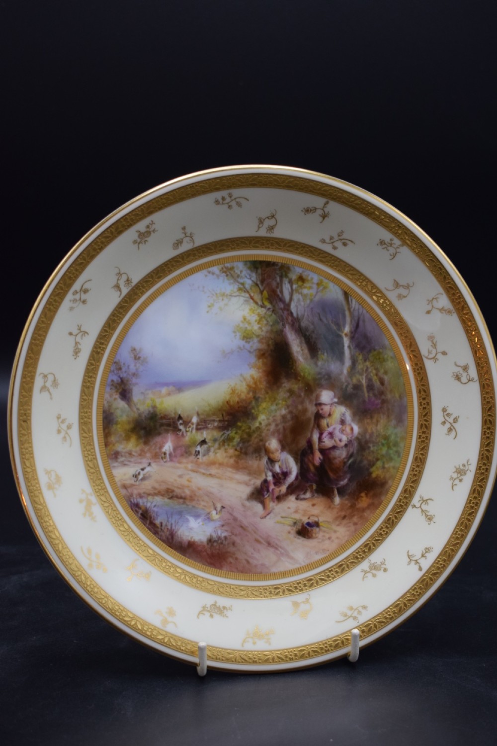 A pair of circular porcelain plates decorated with hand-painted pastoral landscapes and framed by wide cream borders with intricate gilded detailing. View IV