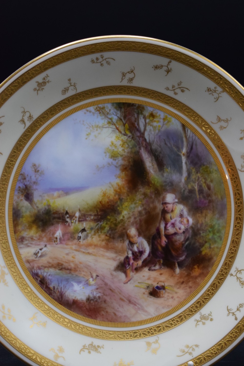 A pair of circular porcelain plates decorated with hand-painted pastoral landscapes and framed by wide cream borders with intricate gilded detailing. View V
