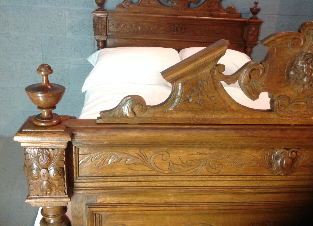 An antique French Breton oak double bed frame featuring intricate relief carvings, barley twist column accents, and decorative cresting on the headboard and footboard. View IX