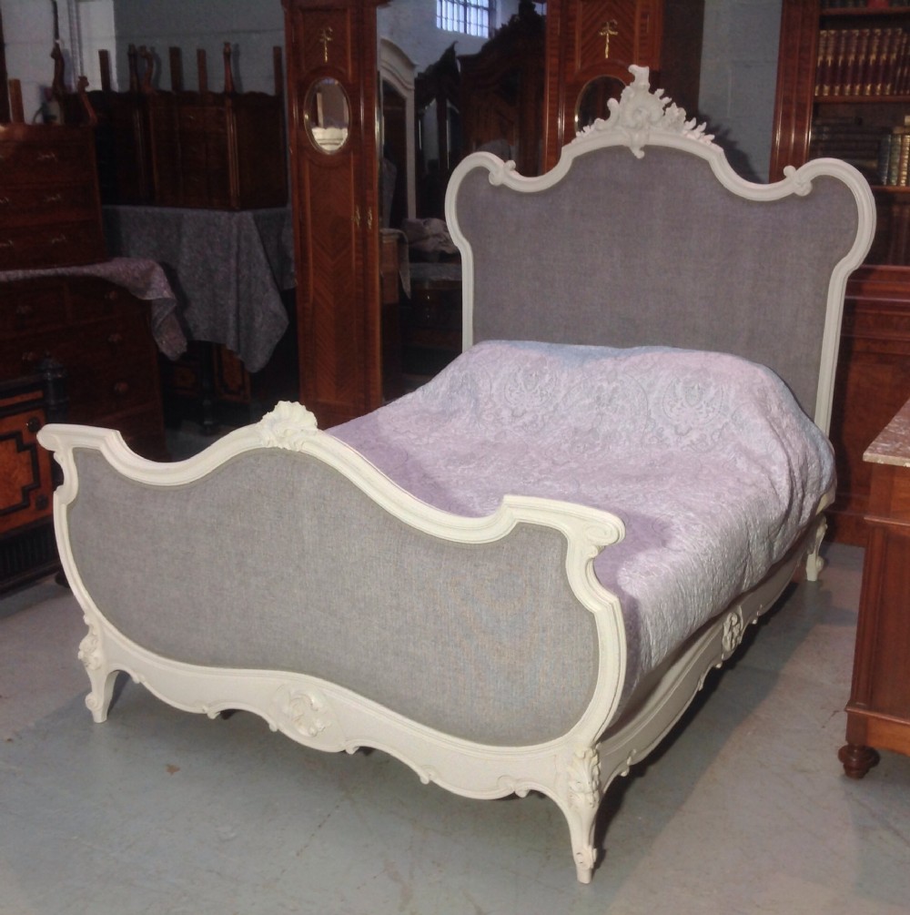 A French Louis XV style king-size bed featuring a carved off-white wooden frame with grey fabric upholstery on the headboard and footboard. View X
