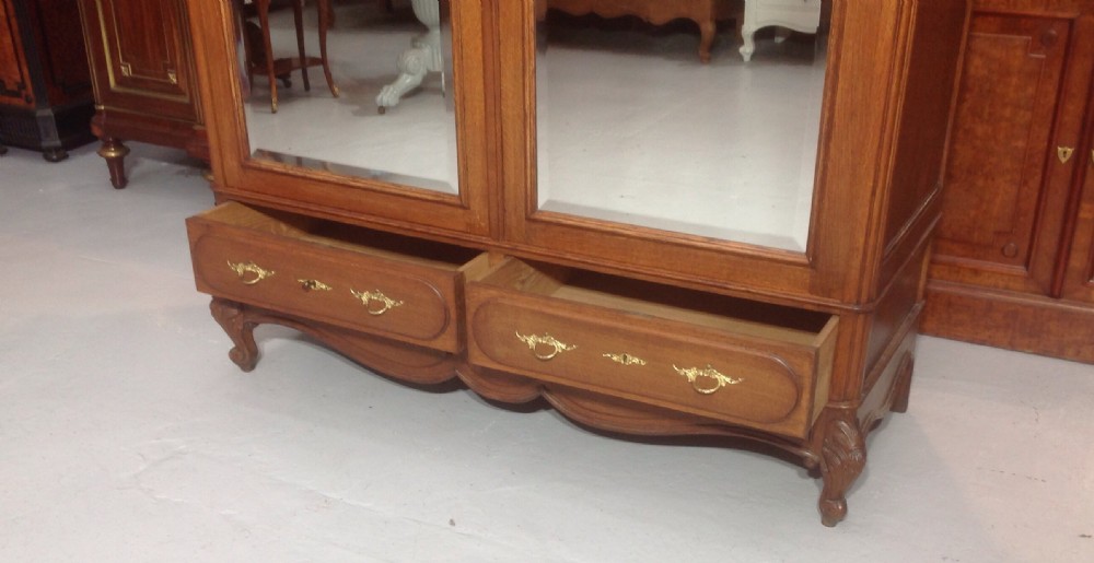 A tall French provincial carved oak armoire with two full-length mirrored doors, an arched cresting pediment, base drawers, and cabriole feet. View IV