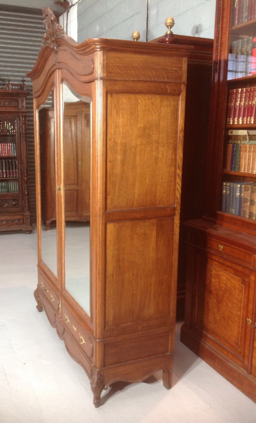 A tall French provincial carved oak armoire with two full-length mirrored doors, an arched cresting pediment, base drawers, and cabriole feet. View VI