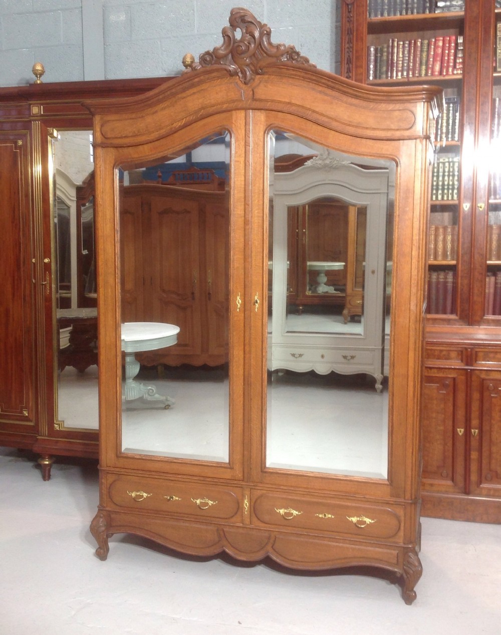 A tall French provincial carved oak armoire with two full-length mirrored doors, an arched cresting pediment, base drawers, and cabriole feet. View VIII