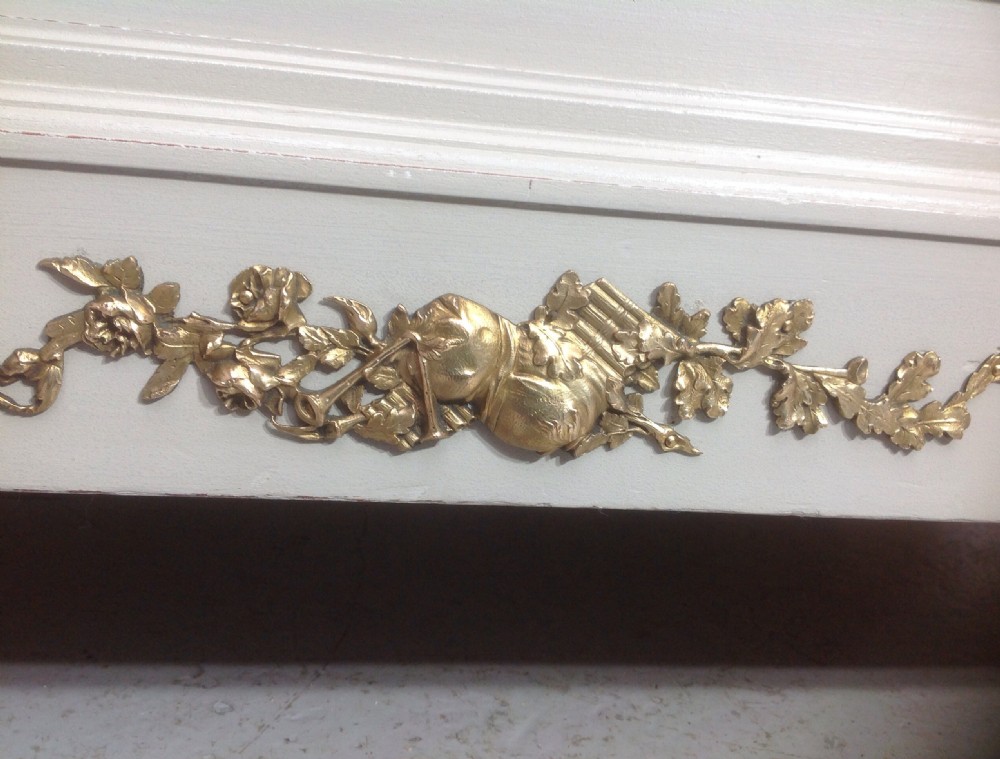 An off-white painted French Neoclassical bed frame featuring a tall rectangular headboard, fluted turned legs, and intricate brass swag mounts on the footboard. View V