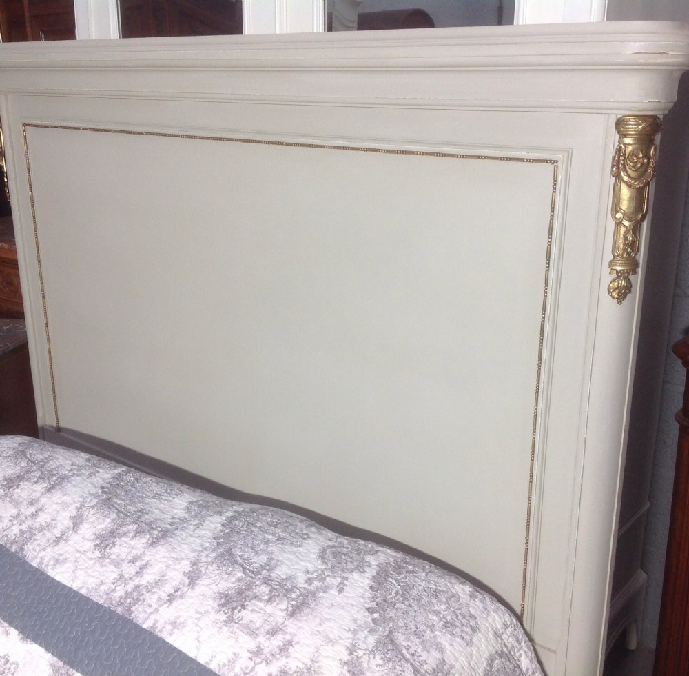 An off-white painted French Neoclassical bed frame featuring a tall rectangular headboard, fluted turned legs, and intricate brass swag mounts on the footboard. View XI