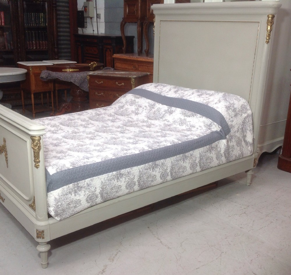 An off-white painted French Neoclassical bed frame featuring a tall rectangular headboard, fluted turned legs, and intricate brass swag mounts on the footboard. View XIII