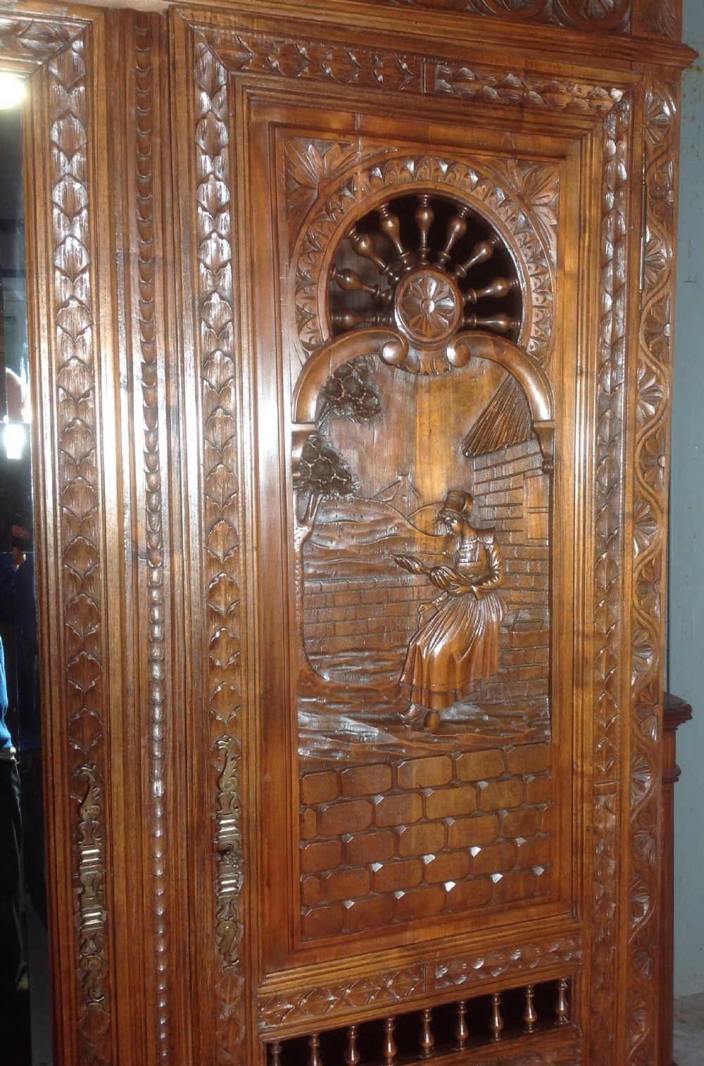 A tall carved walnut Breton armoire featuring one full-length mirrored door and one timber door with detailed relief carving and a spindle gallery. View II