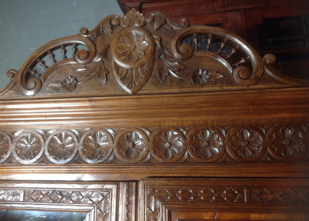 A tall carved walnut Breton armoire featuring one full-length mirrored door and one timber door with detailed relief carving and a spindle gallery. View V
