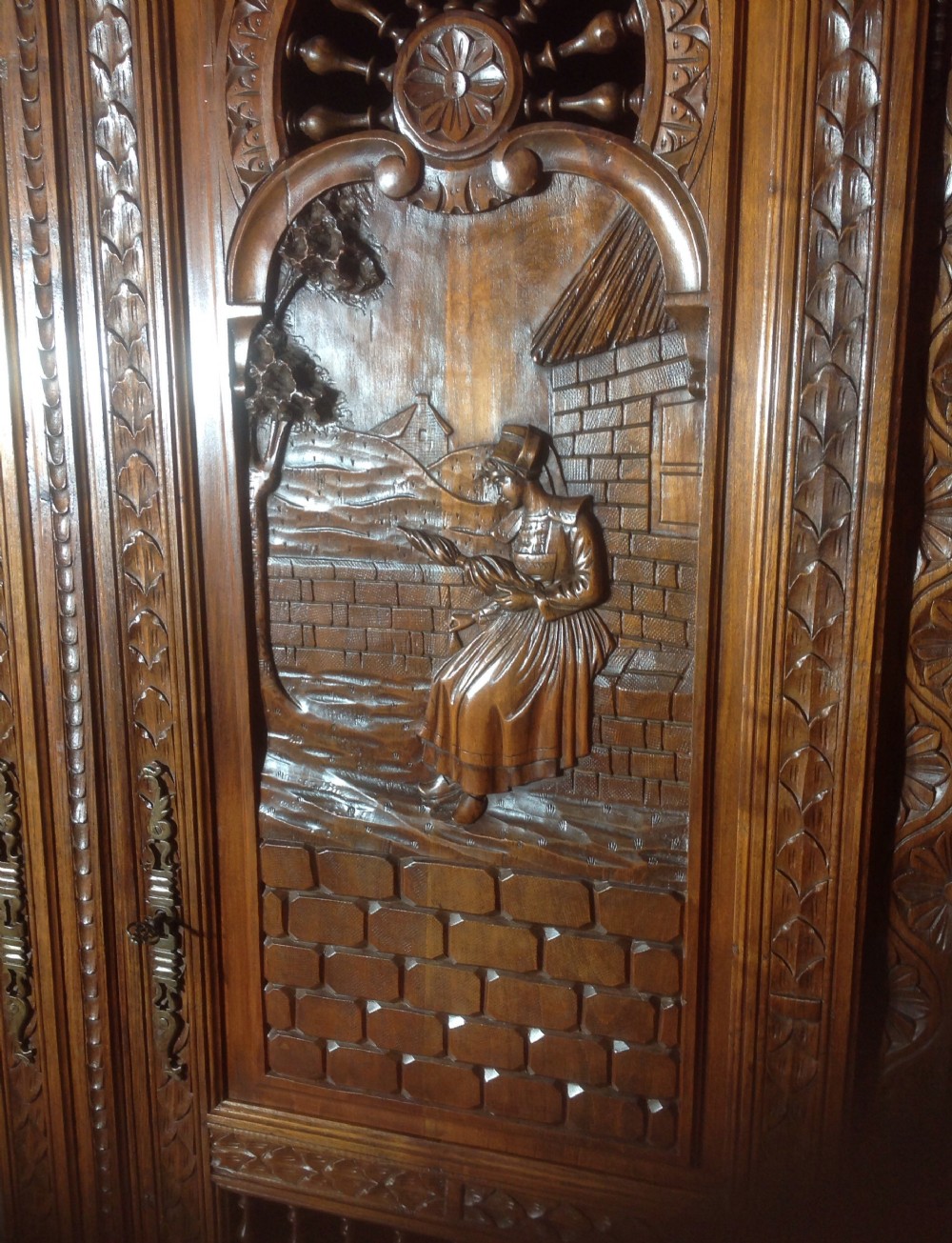 A tall carved walnut Breton armoire featuring one full-length mirrored door and one timber door with detailed relief carving and a spindle gallery. View VII