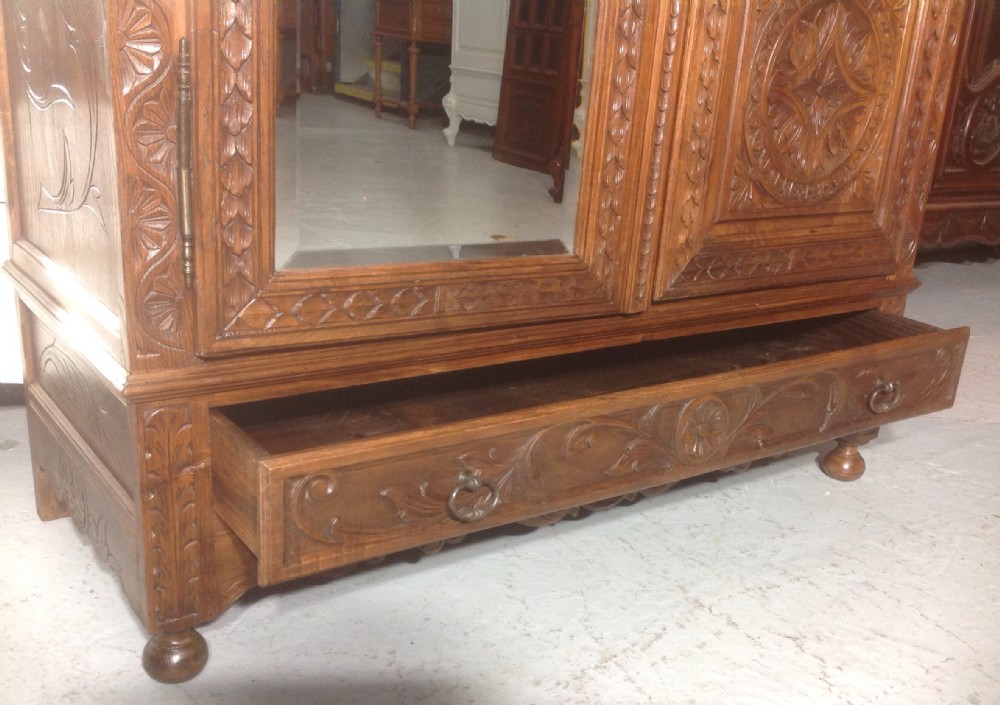 A tall carved walnut Breton armoire featuring one full-length mirrored door and one timber door with detailed relief carving and a spindle gallery. View IX