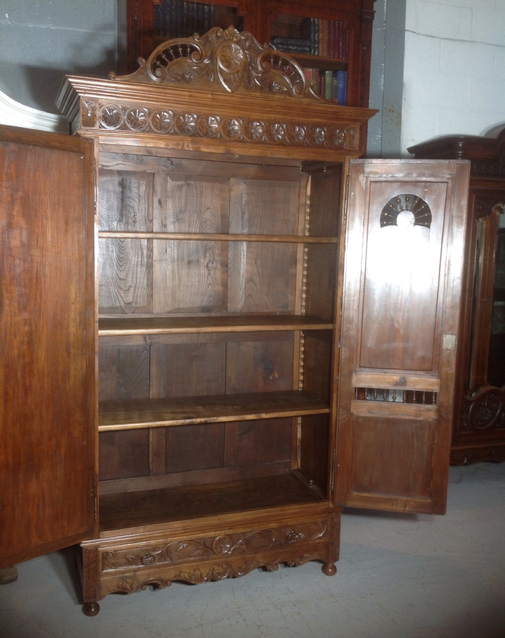 A tall carved walnut Breton armoire featuring one full-length mirrored door and one timber door with detailed relief carving and a spindle gallery. View X