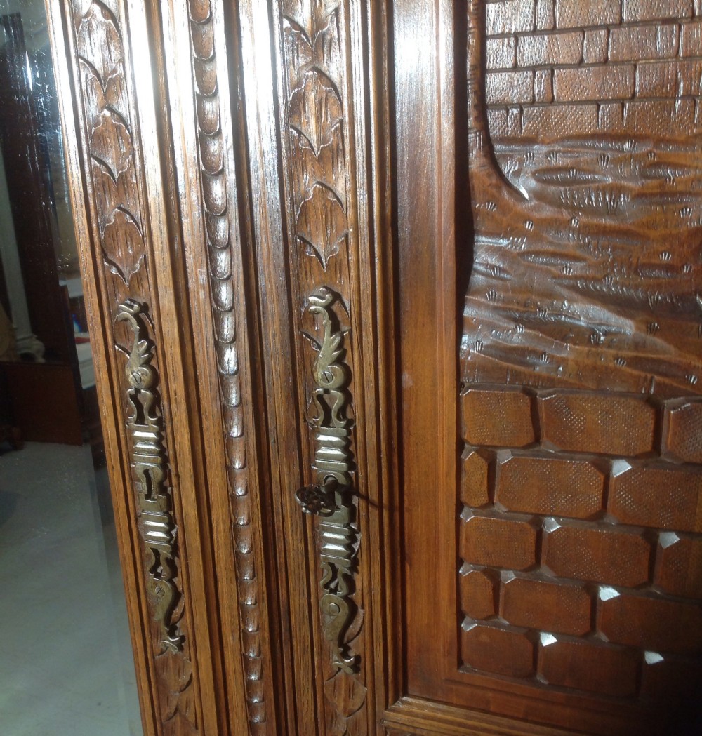 A tall carved walnut Breton armoire featuring one full-length mirrored door and one timber door with detailed relief carving and a spindle gallery. View XI