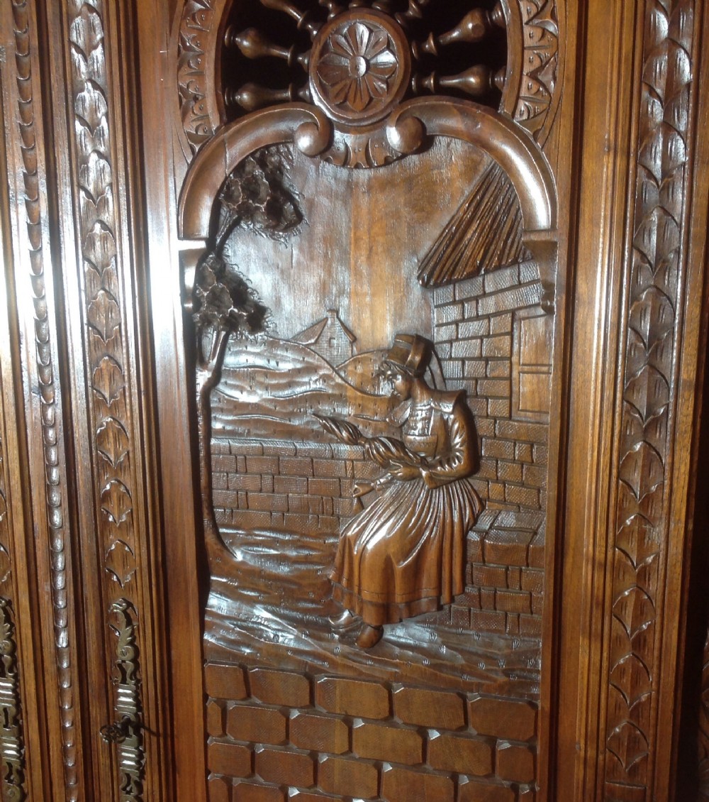 A tall carved walnut Breton armoire featuring one full-length mirrored door and one timber door with detailed relief carving and a spindle gallery. View XII