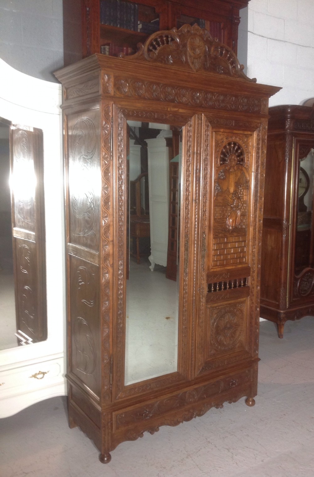 A tall carved walnut Breton armoire featuring one full-length mirrored door and one timber door with detailed relief carving and a spindle gallery. View XIII