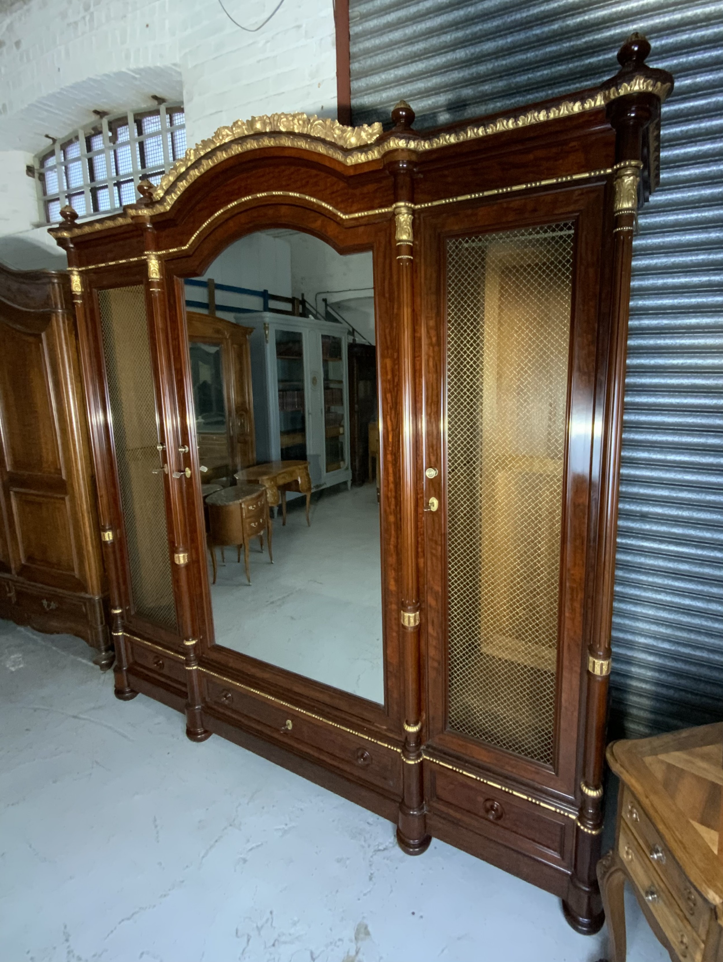 A large mahogany three-door armoire featuring a central arched mirrored door, wire-mesh side panels, and gilt bronze mounts. View II