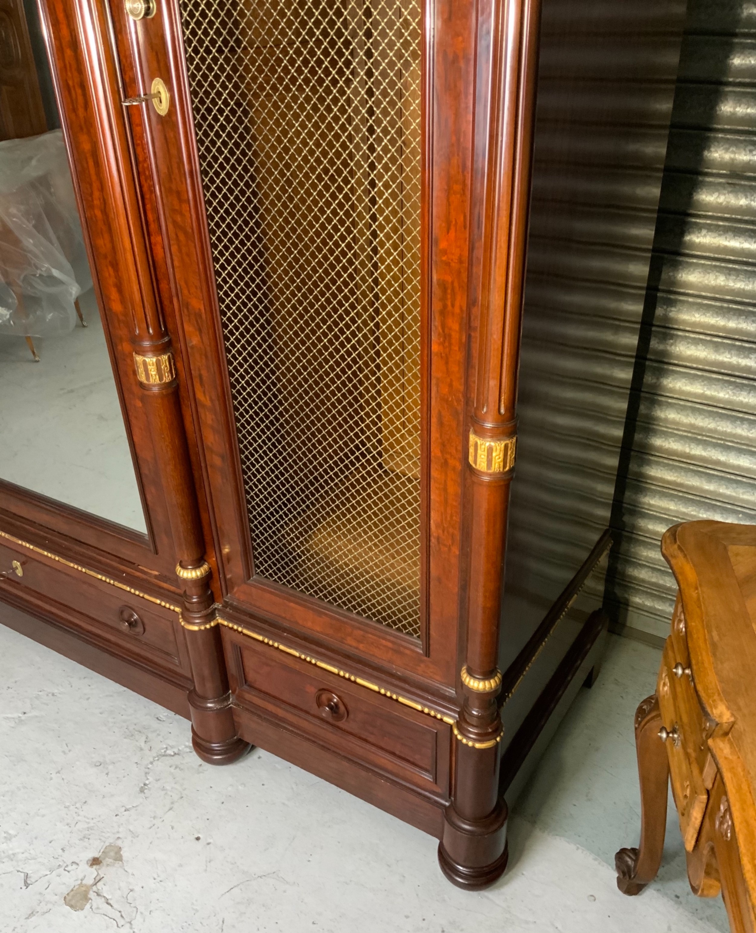 A large mahogany three-door armoire featuring a central arched mirrored door, wire-mesh side panels, and gilt bronze mounts. View VII
