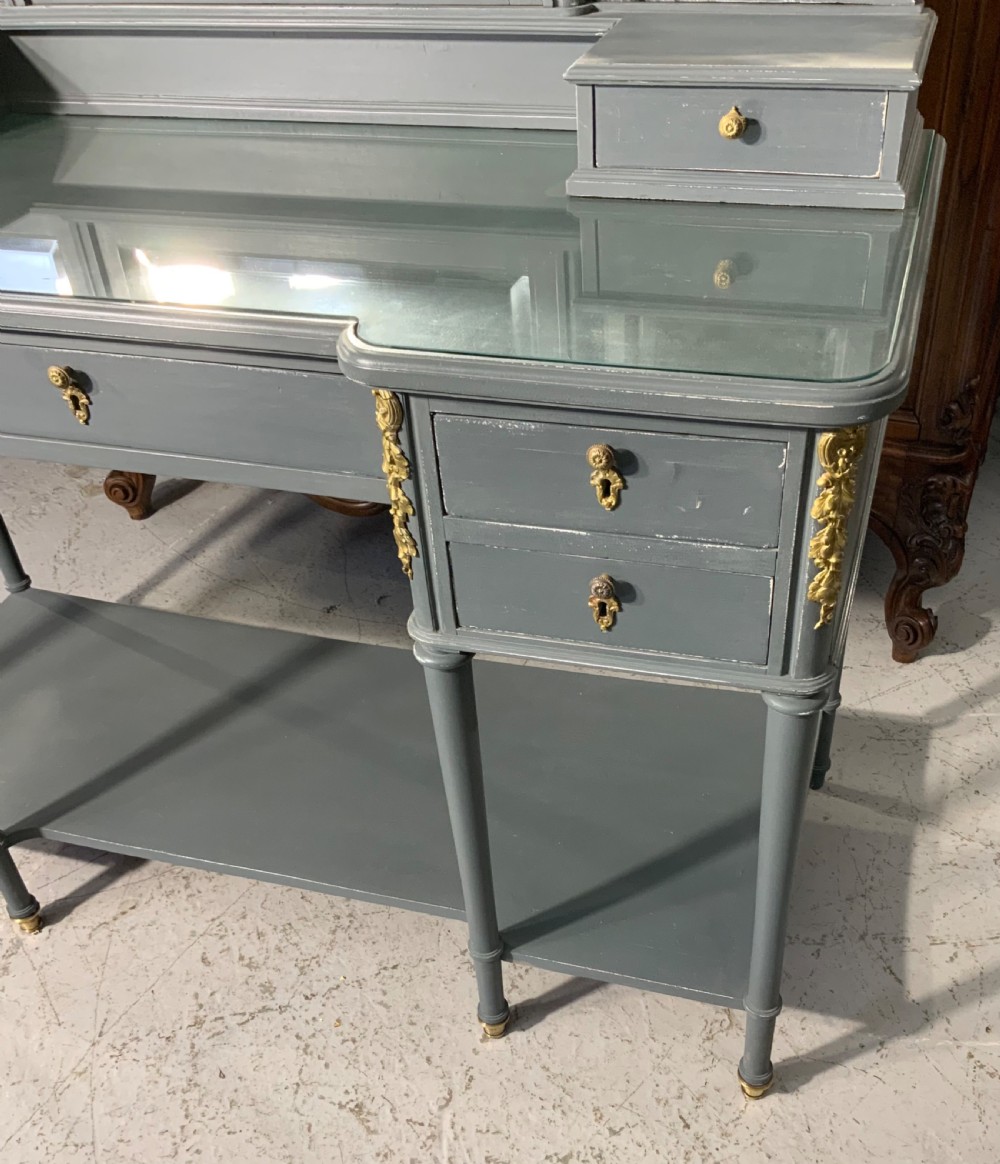 A plummet grey painted French dressing table featuring a central tri-fold mirror, brass embellishments, a glass top, multiple drawers, and turned legs. View II
